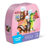 Crocodile Creek puzzle packaging with cartoon animals and cakes on a pink background