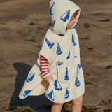 Child wearing a hooded towel with blue sailboat pattern on a sandy beach