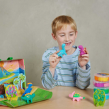 Child playing with colourful clay dinosaur toys on a table against a plain background