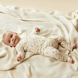 Baby lying on back on floor wearing WILSON & FRENCHY Bella Floral Organic Zipsuit With Feet