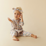 Baby sitting on floor wearing WILSON & FRENCHY Tiny Bloom Organic Zipsuit With Feet & matching headband