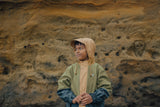Child standing in front of a rock wearing the CRYWOLF Explorer Jacket - Fern Colourblock - Green, Black & Tan raincoat