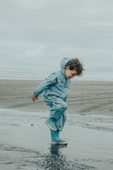 Side view of child splashing at beach wearing CRYWOLF Splash Suit - Stone Blue and matching gumboots