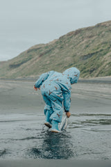 Back view of child wearing CRYWOLF Splash Suit - Stone Blue & matching rainboots at the beach