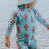Child wearing blue swimsuit with all over red lobster pattern in the water