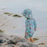 Child wearing a blue swimsuit with red patterns and matching hat on a beach.