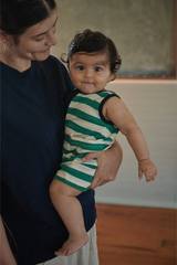 Woman holding a baby wearing a green and white striped outfit indoors.