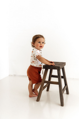 Child standing next to a wooden stool against a white background
