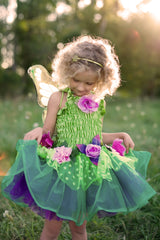 Child in a fairy costume with wings and flowers standing in a grassy field.