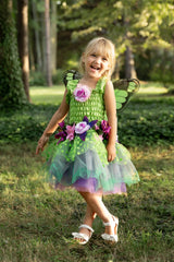 Child in a green fairy costume with wings and flowers, standing in a grassy outdoor setting.