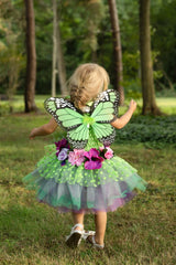 Back view of a child in a green butterfly costume with a tutu standing in a forest.