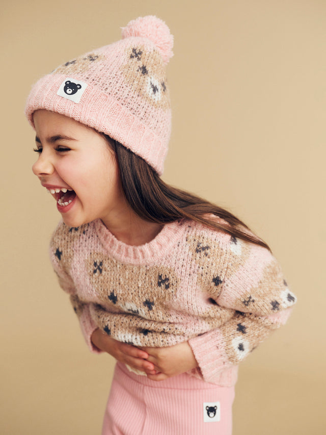 Studio image of child wearing the HUXBABY Rosebud Huxbear Knit Jumper and matching beanie