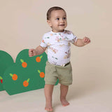 Baby standing on a beige floor with a green treetop-shaped backdrop featuring orange fruits.