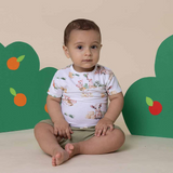 Baby sitting on a beige surface with a green backdrop featuring orange and red shapes.