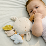 Baby lying on a white blanket with a plush toy and teething ring.