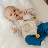 Baby holding a plush toy with 'Dream Big Little One' text on a white background