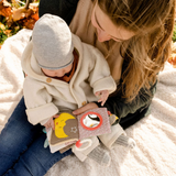 Woman holding a baby and a soft book outdoors in autumn