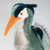 Detailed view of stuffed toy pelican with an orange beak and green body on a light gray background