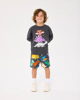 Studio shot of boy wearing ROCK YOUR BABY DINO STACK LONG SLEEVE T-SHIRT and the multi-coloured dinosaur shorts