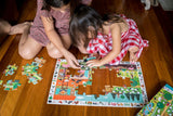 Two children playing with a puzzle on a wooden floor
