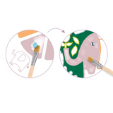 Illustration of a pink elephant being painted with green and yellow details, surrounded by paintbrushes and colour swatches.