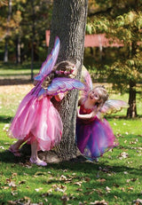 Two children in fairy costumes standing next to a tree in a park.