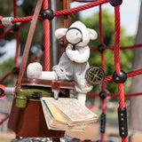 Plush toy sheep wearing tweed overalls looking through a magnifying glass while sitting in a playground structure
