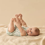 Baby lying on a beige blanket wearing a floral onesie.