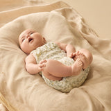 Baby lying on a soft beige blanket wearing a onesie with lemon leaf pattern.