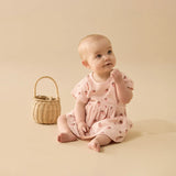 Baby in a pink dress sitting next to a wicker basket on a beige background