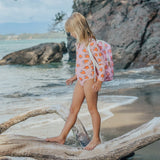 Woman in a pink swimsuit with orange hearts standing on a log at the beach.