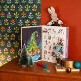 Decorative setup with an open Christmas-themed Advent Calendar, small decorative trees, and a rabbit and elephant figurine on a wooden surface.