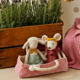 Two plush toys in a pink basket with a wooden planter and pink blanket in the background