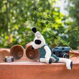 Stuffed dog toy with a camera and plant pots on a wooden surface