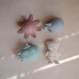 Top view of four silicone bath toys on a light surface with shadows