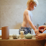 Child playing with silicone bath toys in a bathtub, with adult hands assisting.