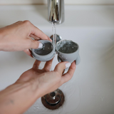 Person holding two halves of a silicone bath toy under running water in a sink.
