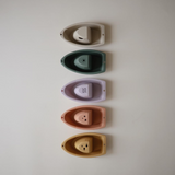 Five small boat-shaped toys in different colours arranged vertically on a light gray background.
