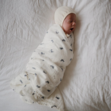 Newborn baby wrapped in a white swaddle with blue whale patterns on a white blanket.