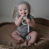 Baby in a bunny costume chewing a bunny teething ring on a textured surface