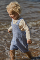 Child in blue overalls playing in water near a body of water