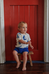 Child sitting on a wooden stool in front of a red door