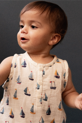 Baby wearing a sleeveless romper with sailboat pattern against a dark background