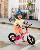 Child riding a balance bike on a sidewalk with a helmet and knee pads.