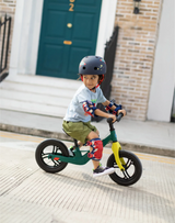 Child riding a balance bike on a sidewalk with a building in the background
