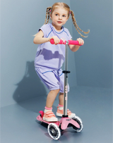 Young girl riding a pink scooter against a plain background