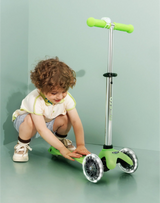 Child playing with a green scooter on a light green background