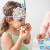 Child wearing a butterfly-themed crown eating a decorated cookie.