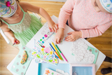 Two children coloring at a table with crayons and coloring books.