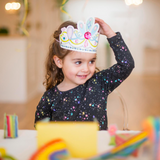 Child wearing a colorful paper crown indoors with a blurred background